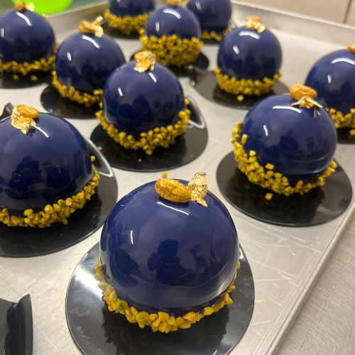 Dunkelblaue Pistazie-Himbeer-Litschi Törtchen mit Mirror Glaze und Blattgold. Handgemachte Monoportionen in Leipzig von Kuchenexpress24.de.